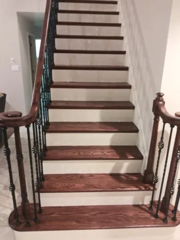 A wooden staircase with white steps and a wrought iron railing in a house.