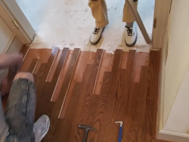 A person is working on a wooden floor with a hammer